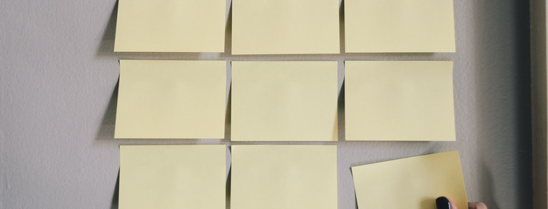 Gelbe Haftnotizzettel, die in drei Reihen à drei Zettel auf eine weiße Fläche geklebt sind