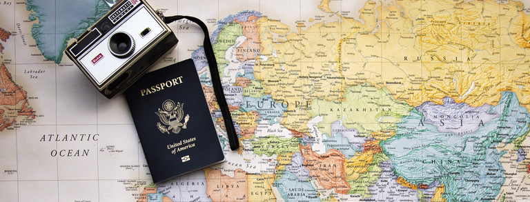 Bunde Weltkarte, im Zentrum Europa, auf der ein schwarzer Reisepass sowie eine silberne Kompaktkamera liegen