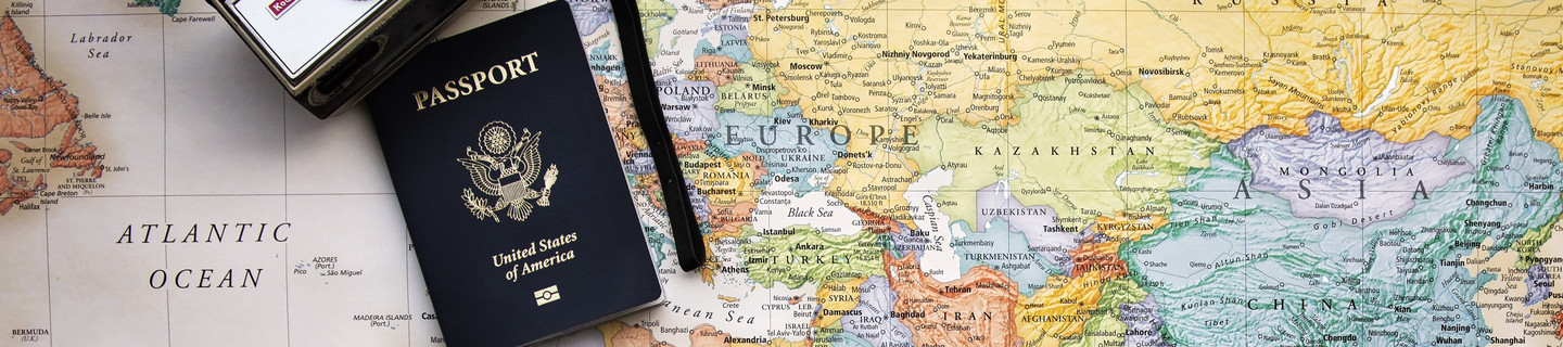 Bunde Weltkarte, im Zentrum Europa, auf der ein schwarzer Reisepass sowie eine silberne Kompaktkamera liegen