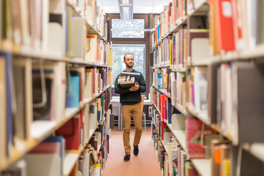 Student walks along the bookshelves in the library.