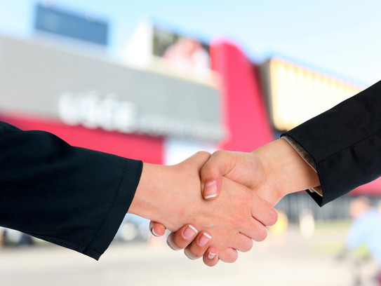 Two shaking hands. A building and a blue sky can be seen in the background.