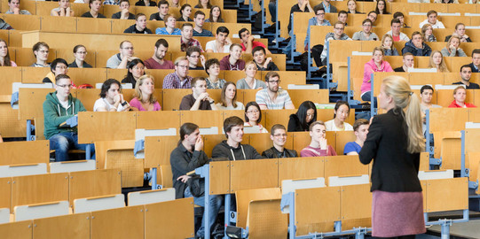 Eine Dozierende steht vor Studierenden in der Vorlesung im Hörsaal. 